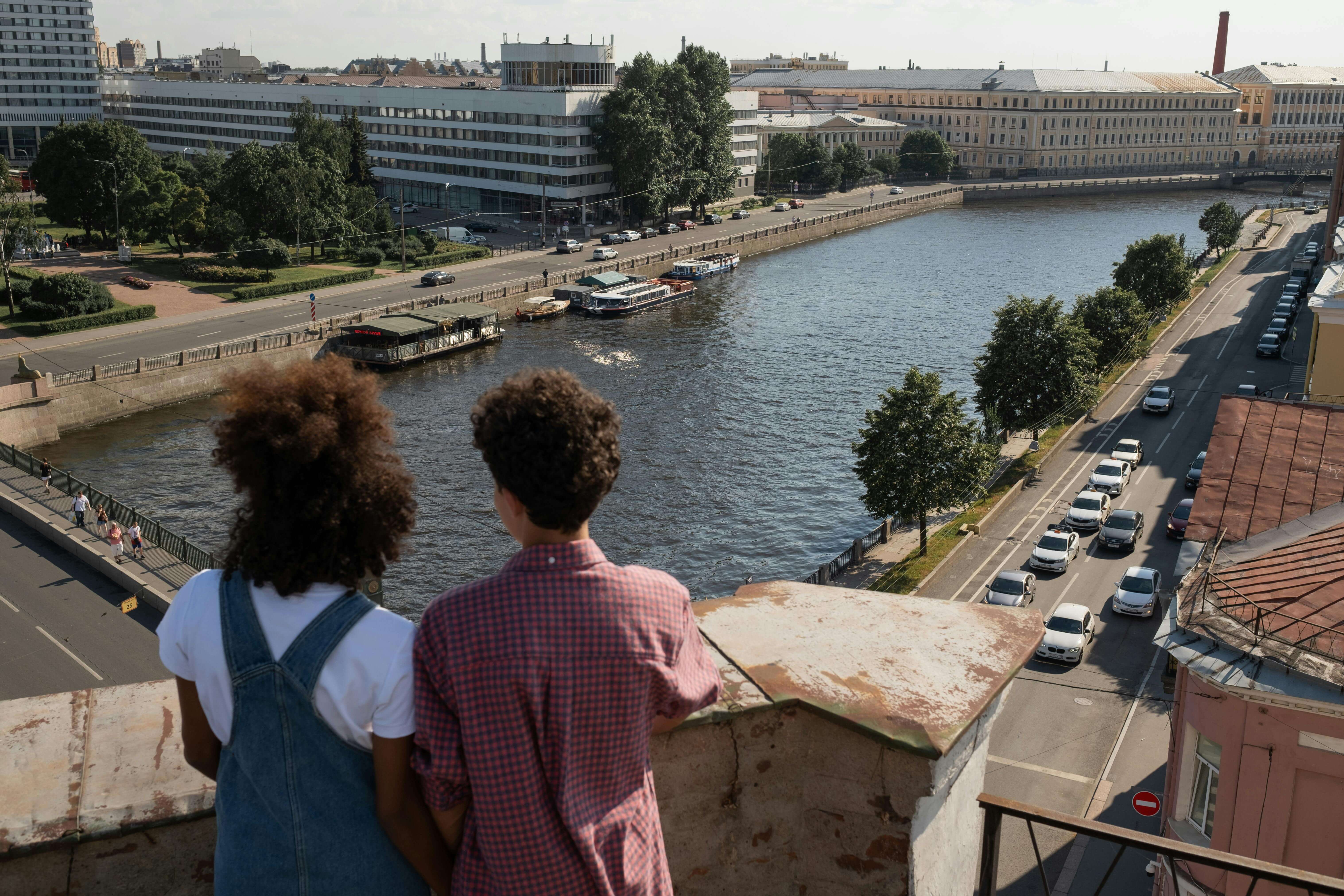 Young couple enjoying a scenic view of the city and river from a rooftop on a sunny day.