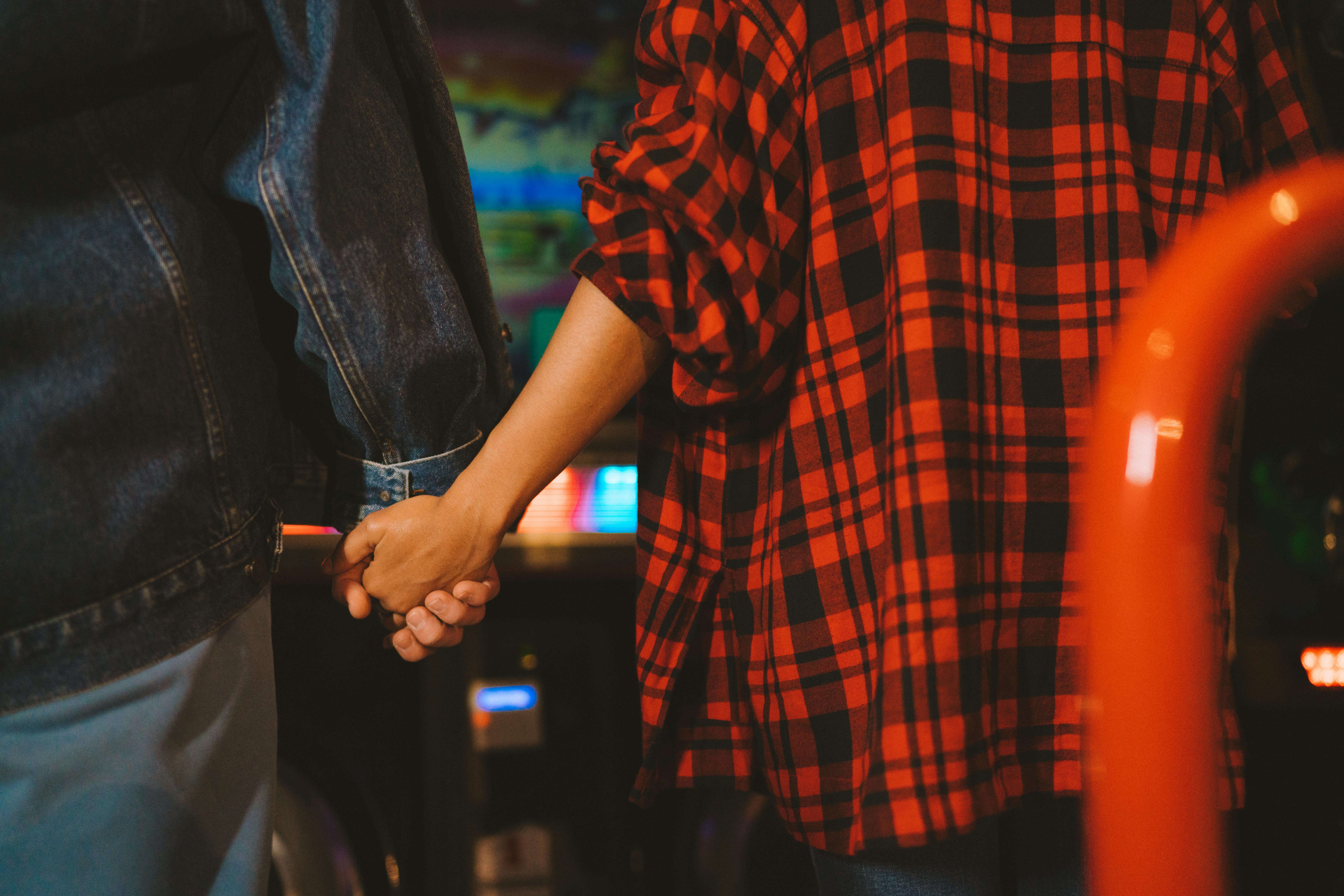 Romantic moment captured with a couple holding hands in a vibrant arcade environment.