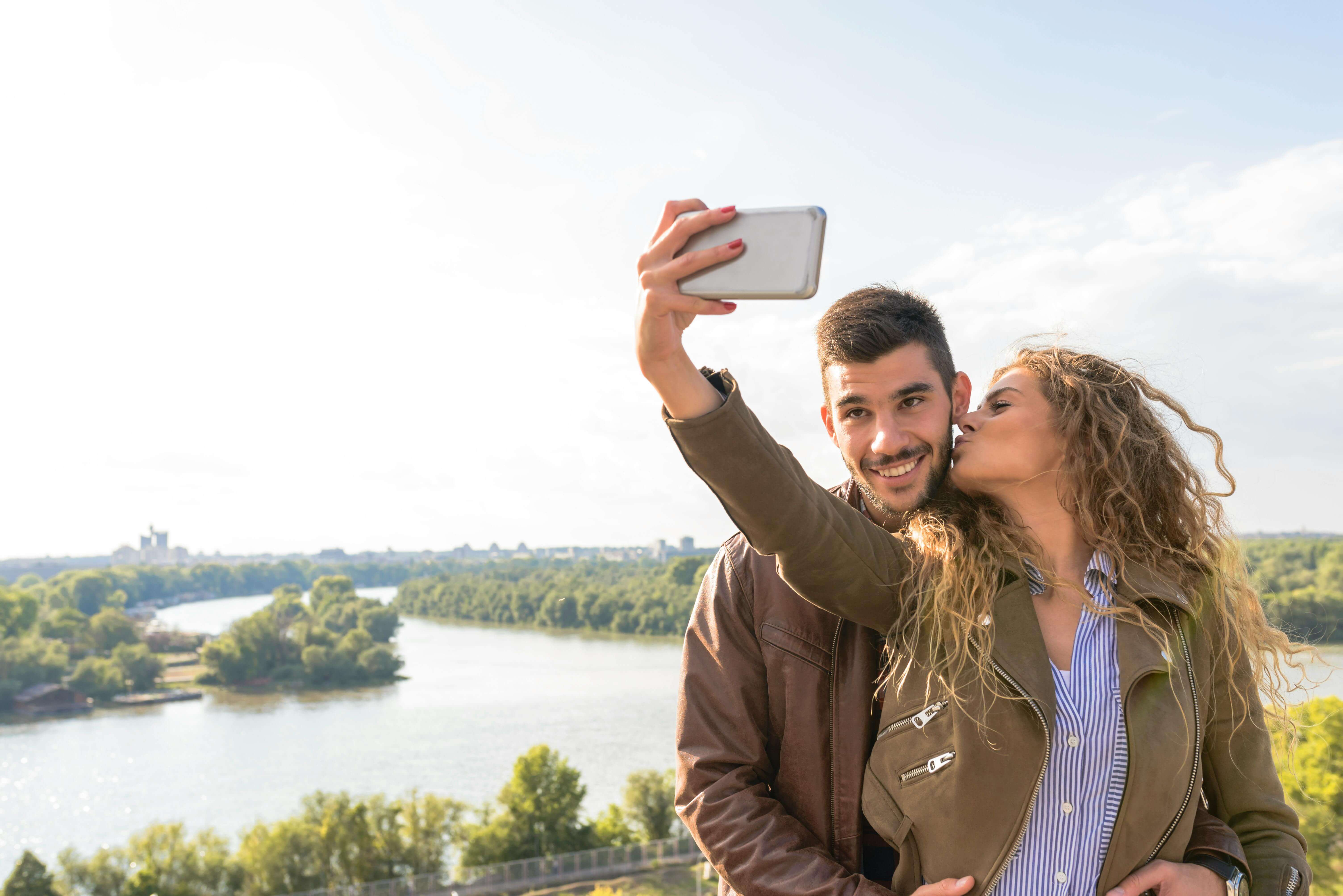 Happy couple enjoying a moment by the river, capturing a selfie to cherish their travel memories.
