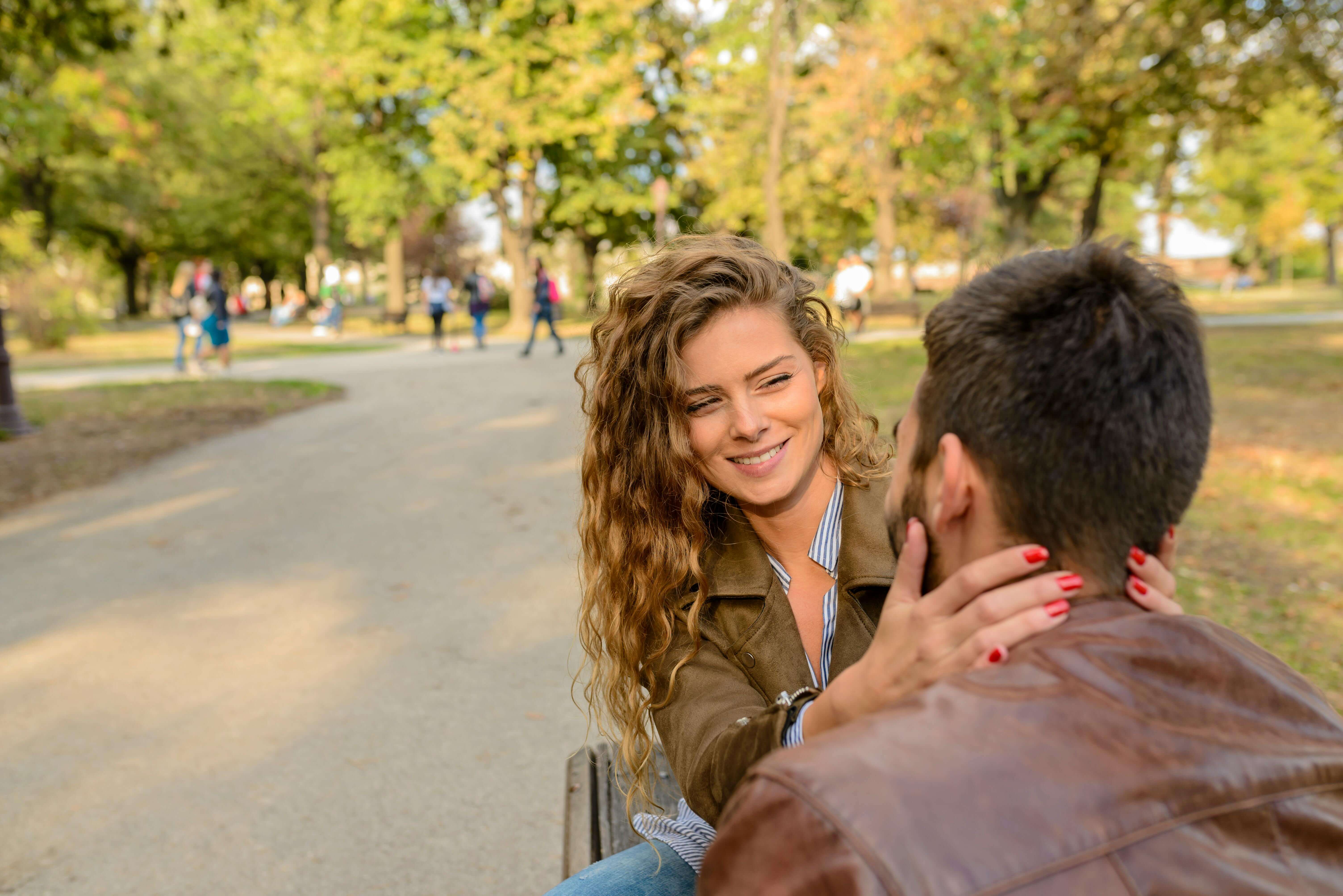 Young couple enjoying a loving moment outdoors in a sunny park setting.