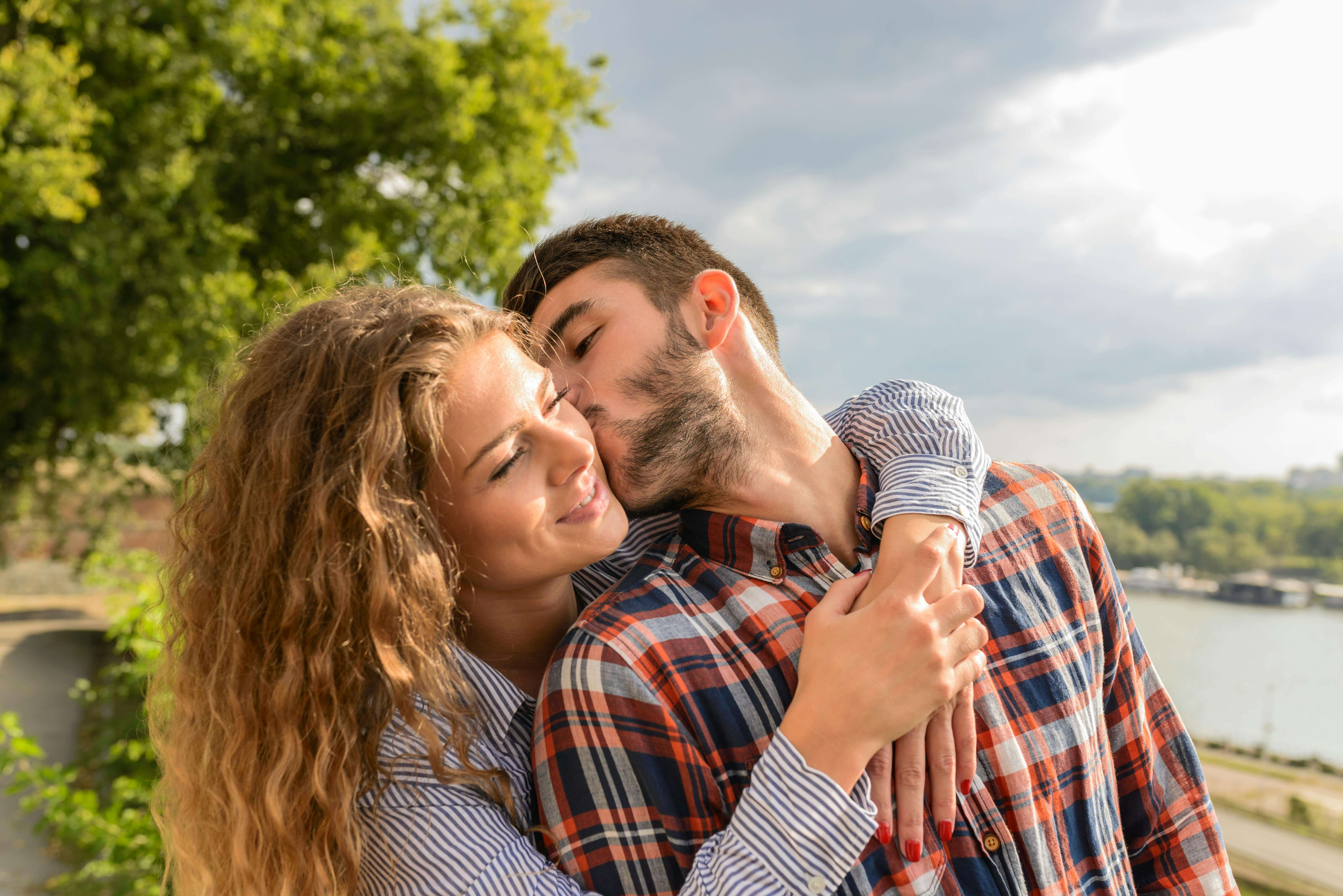 Happy couple sharing a loving embrace outdoors with a scenic background.