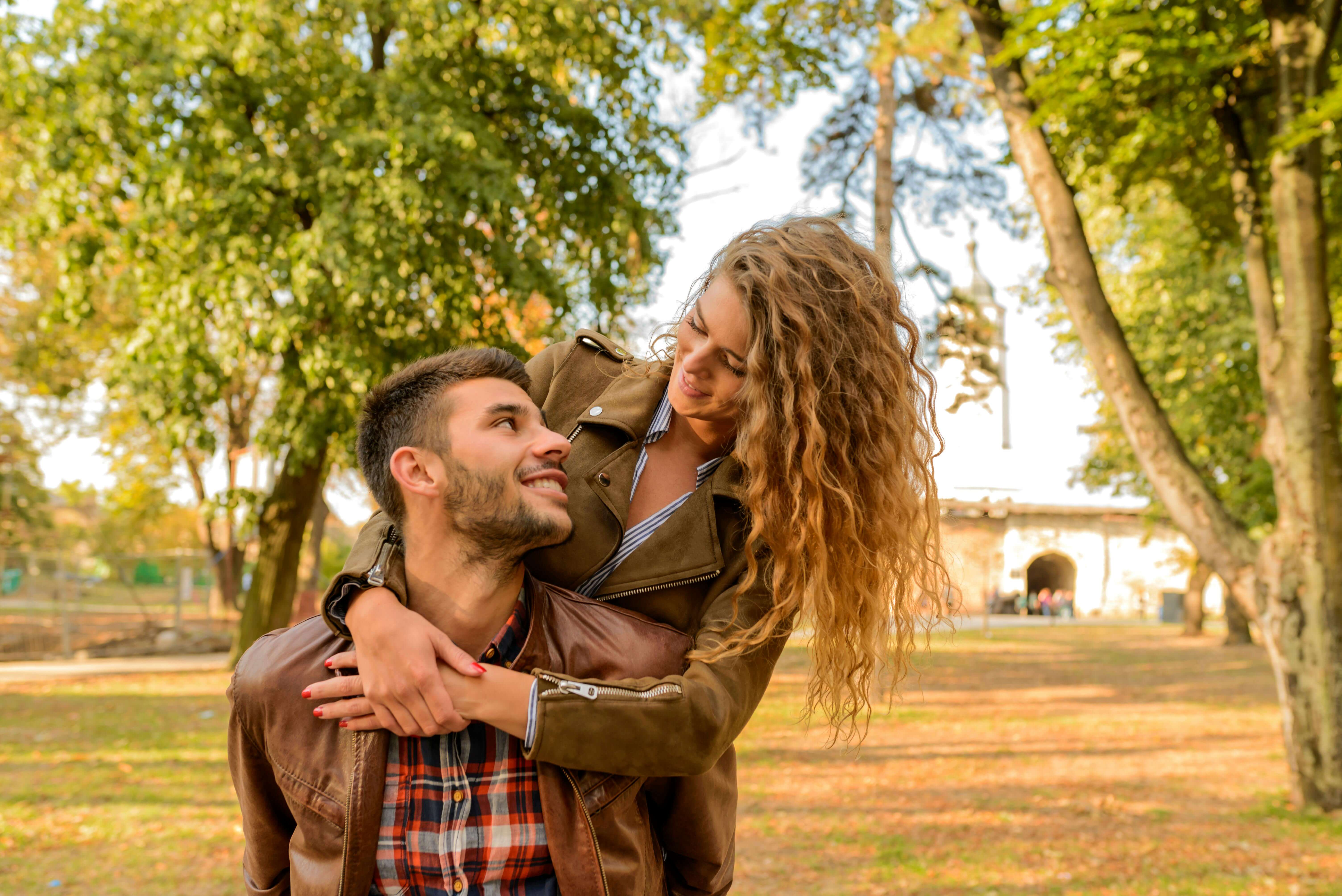 Smiling couple embracing in a sunlit park during fall, capturing love and joy.