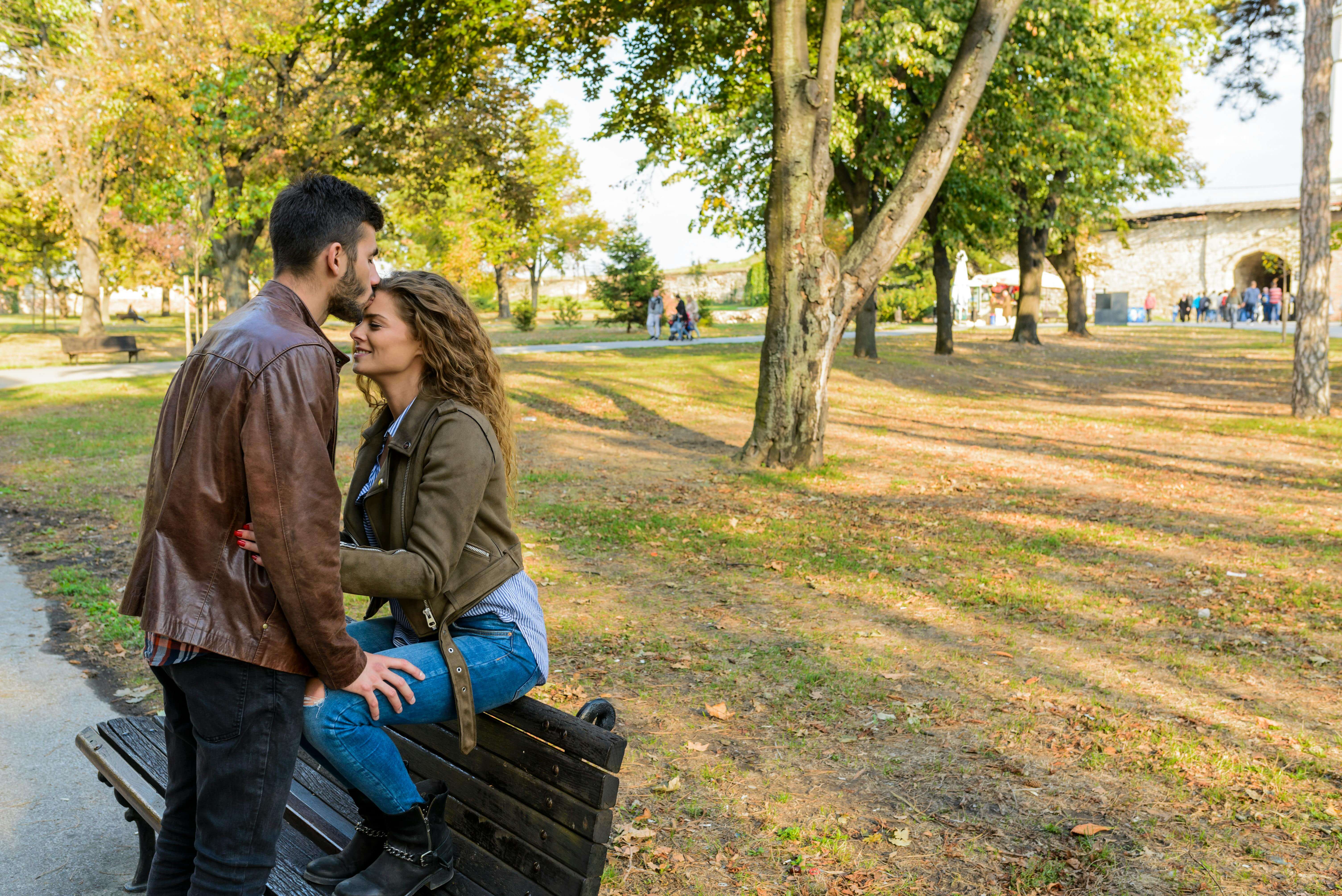 A loving couple enjoys a tender moment on a park bench surrounded by autumn trees.