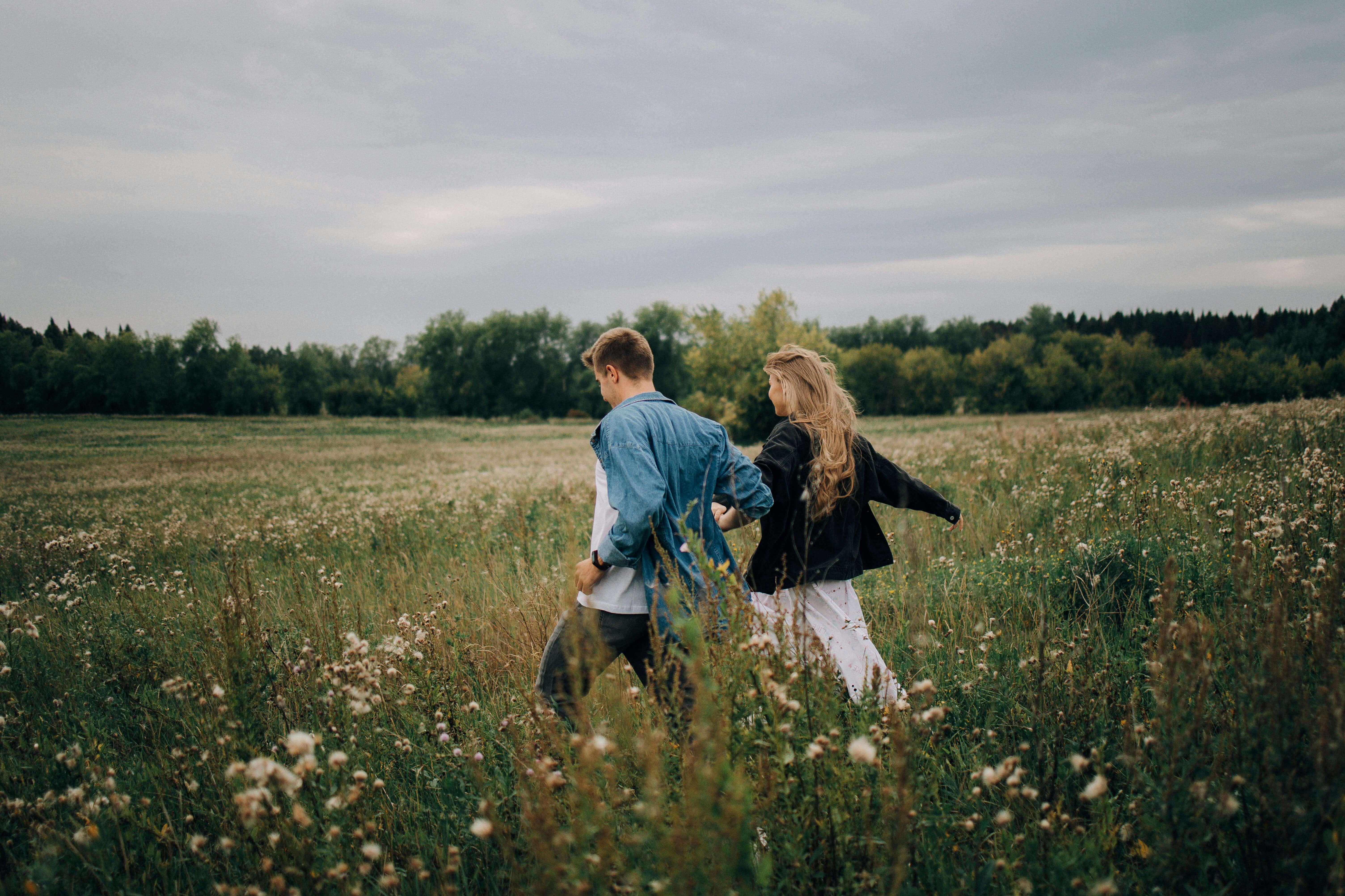 A couple in love holds hands while walking through a summer field, surrounded by nature.